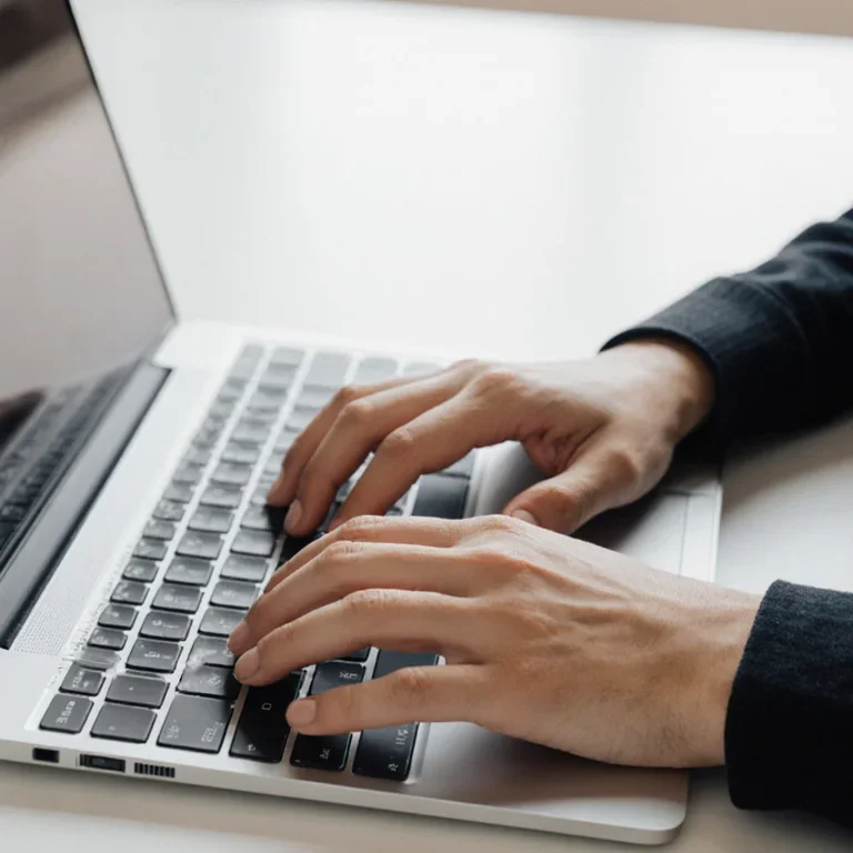 Close-up of a sole proprietor's hands typing on a laptop keyboard, preparing a freelance invoice using their personal name.
