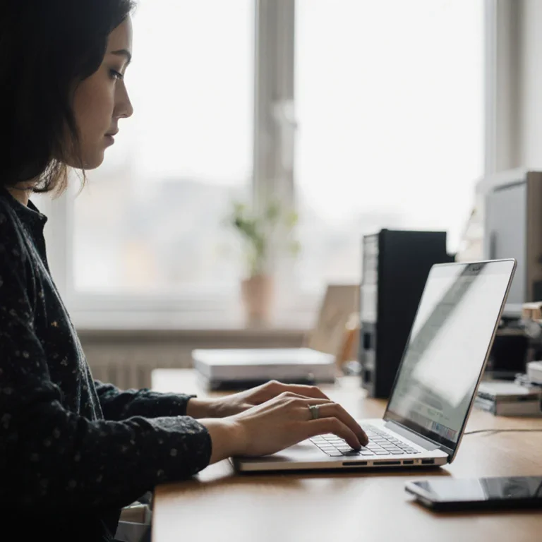 A person working from a home office, carefully entering details into an online invoice creator on their laptop.